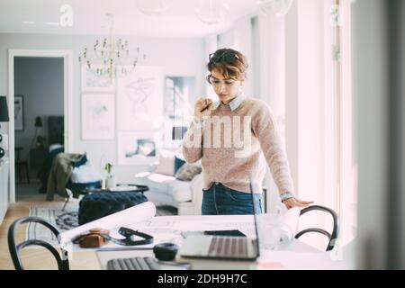 Frau, die am Tisch steht, mit Blaupause, die zu Hause arbeitet Stockfoto