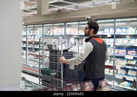 Rückansicht des Verkäufers, der den Wagen mit Kunststoffkisten schiebt Im Supermarkt Stockfoto