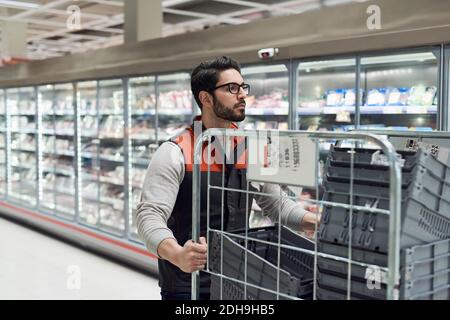 Verkäufer schiebt Wagen mit Kunststoffkisten an Kühlteil Im Supermarkt Stockfoto