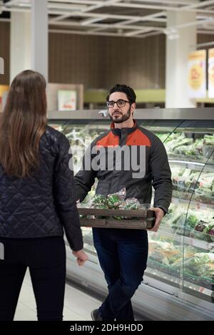 Rückansicht einer Frau, die mit einem männlichen Verkäufer im Gespräch war Paprika in der Kiste im Supermarkt Stockfoto