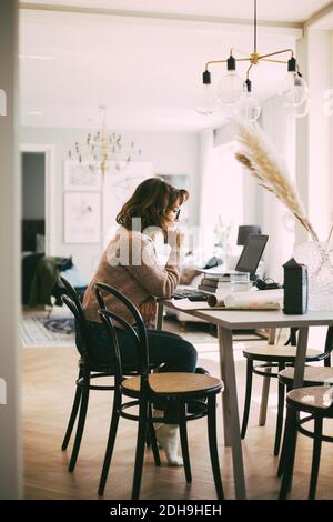 Frau, die zu Hause am Tisch sitzt und mit Kollegen spricht Online-Meeting Stockfoto