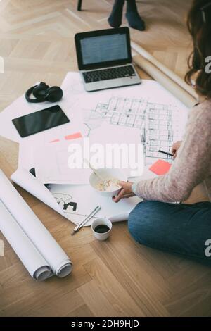 Frau, die auf dem Boden saß und Blueprints beim Frühstück ansah Stockfoto