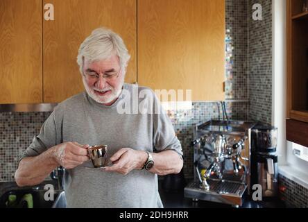 Lächelnder älterer Mann, der die Kaffeetasse hält, während er in der Küche steht Zähler Stockfoto