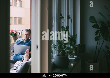 Mann, der am Laptop arbeitete und auf dem Balkon relaxte Stockfoto