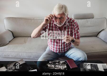 Älterer Mann, der auf dem Sofa sitzend Vintage-Fotos ansieht Zu Hause Stockfoto