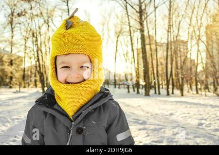 Junge lächelte und kielte auf die Sonne. Winter, Park, Kopierplatz. Nahaufnahme im Hochformat. Farbe 2021, gelb und grau. Stockfoto