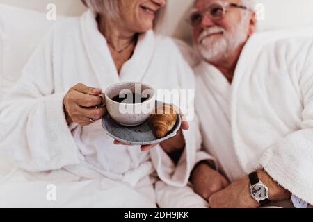Ein älterer Mann sah eine Frau an, die Kaffee auf dem Bett hielt Hotelzimmer Stockfoto