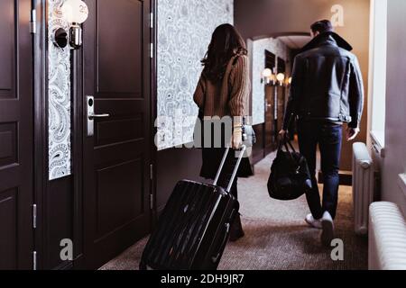 Rückansicht des Paares, das mit Gepäck im Flur läuft Hotelzimmer Stockfoto
