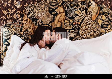 Ein Paar küsst sich, während es im Hotelzimmer auf dem Bett liegt Stockfoto