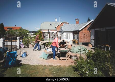 Seitenansicht einer älteren Frau mit Zementmischer, während Mann Spaziergang im Hintergrund auf dem Hof Stockfoto