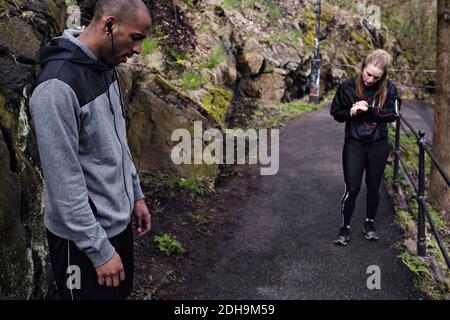 Seitenansicht des müden männlichen Athleten, der auf der Straße mit steht Frau im Hintergrund Stockfoto