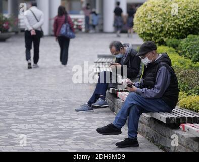 Hongkong, China. Dezember 2020. Bewohner mit Gesichtsmasken sitzen am Straßenrand in Tsim Sha Tsui, Hongkong, Südchina, 10. Dezember 2020. ZU GEHEN MIT "Hong Kong berichtet dreistellige COVID-19 Spitze für 3 aufeinanderfolgende Tage" Credit: Wang Shen/Xinhua/Alamy Live News Stockfoto