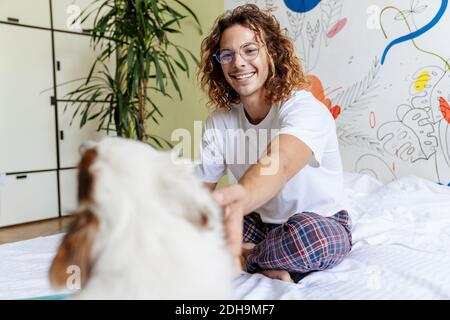 Bild von glücklichen jungen lockigen Mann drinnen zu Hause kuscheln Sein Hund Stockfoto