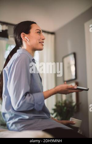 Lächelnder Profi mit Tasse und Handy, die über Kopfhörer sprechen Im Heimbüro Stockfoto