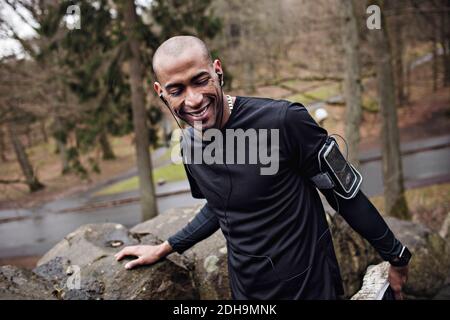 Glücklicher männlicher Athlet, der Musik hört, während er an der Steinwand trainiert Im Wald Stockfoto