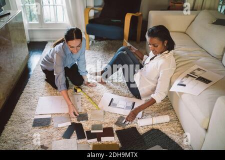 High-Angle-Ansicht der weiblichen Designer diskutieren über Stoffmuster Während Sie im Home Office auf dem Teppich sitzen Stockfoto