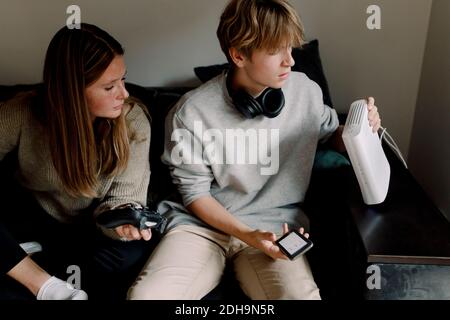 Teenager, der den WLAN-Router überprüft, während er mit einem Freund sitzt Sofa zu Hause Stockfoto