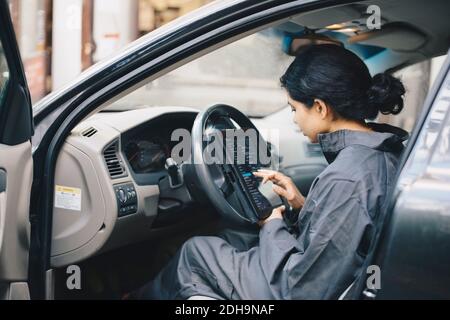 Seitenansicht der weiblichen Mechanikerin mit digitalem Tablet während des Sitzens Im Auto Stockfoto