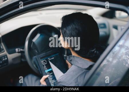 Weibliche Mechanikerin mit digitalen Tablet, während im Auto sitzen Stockfoto