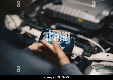 Zugeschnittenes Bild von Mechaniker mit Anwendung auf Smartphone von Öffnen Sie das Fahrzeug Stockfoto