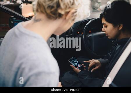 Mechaniker erklärt dem Kunden die Anwendung auf dem Smartphone, während er sitzt Im Auto Stockfoto