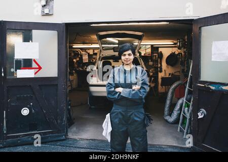 Portrait der selbstbewussten weiblichen Mechanikerin, die am Eingang des Autos steht Reparaturwerkstatt Stockfoto