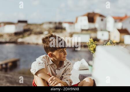 Betrachtend Junge wegschauen, während er draußen während des sonnigen Tages sitzt Stockfoto