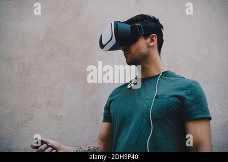 Computerprogrammierer mit VR-Brille und Fernbedienung gegen Beige Wand im Büro Stockfoto