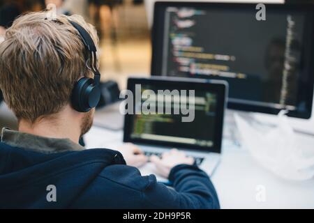 Über die Schulter des Geschäftsmannes, der Kopfhörer während der Programmierung trägt Auf dem Laptop im Kreativbüro Stockfoto