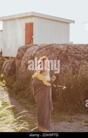 Mutter mit Baby-Mädchen, das weg schaut, während sie bei Felsen steht Bildung Stockfoto