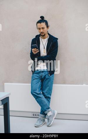 Volle Länge der männlichen Computer-Programmierer mit Smartphone, während Lehnt sich an beigefarbene Wände im Büro Stockfoto
