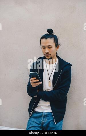 Männliche Computer-Programmierer mit Smartphone, während sich auf beige Wand im Büro Stockfoto