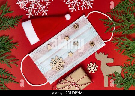 Coronavirus Weihnachten Hintergrund. Gesichtsmaske mit festlichen Verzierungen und grünen Tannenzweigen auf rotem Hintergrund. Weihnachten oder Neujahr Konzept. Flach l Stockfoto