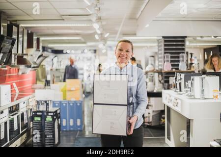 Portrait der lächelnden reifen weiblichen Besitzerin mit Boxen stehen in Elektronikgeschäft Stockfoto