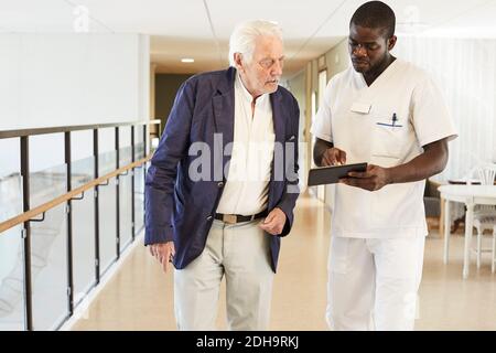 Krankenschwester mit digitalem Tablet und einem älteren männlichen Patienten bei Krankenhausflur Stockfoto