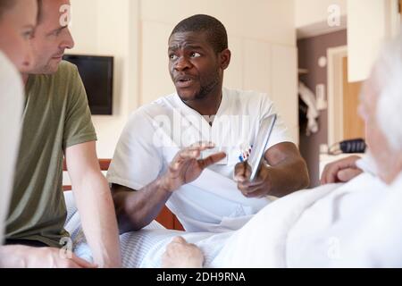 Männliche Krankenschwester über digitale Tablette mit Paar diskutieren, während Senior Mann, der auf der Krankenstation liegt Stockfoto