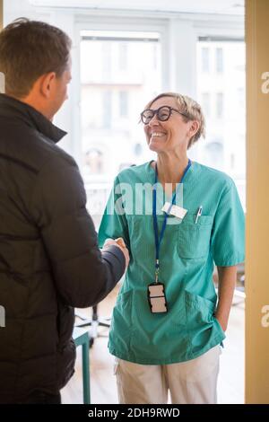 Lächelnde Ärztin schüttelt sich die Hände mit reifen Patienten im Stehen In der Klinik Stockfoto