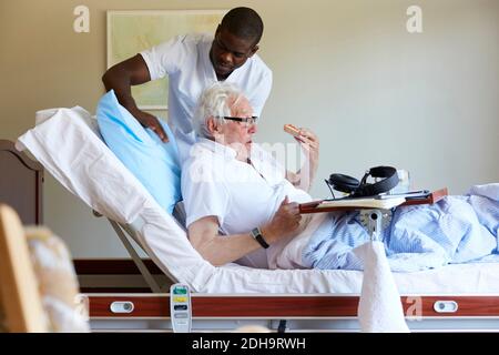 Männliche Krankenschwester Anpassung Kissen für ältere Mann auf Bett in Krankenhausstation Stockfoto