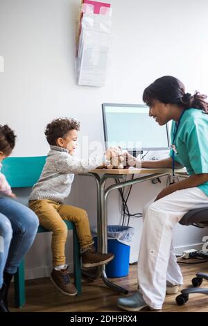 Junge im Gespräch mit lächelnden Krankenschwester beim Spielen mit gefüllt Spielzeug in der Klinik Stockfoto