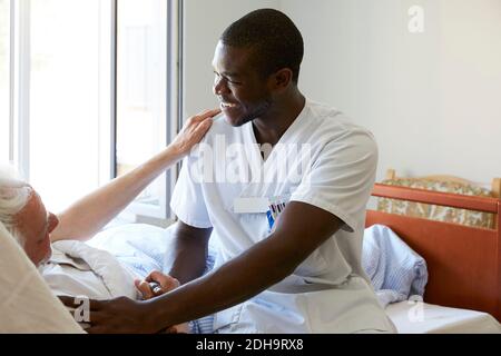 Lächelnde Krankenschwester tröstet älteren Mann auf der Krankenstation Stockfoto