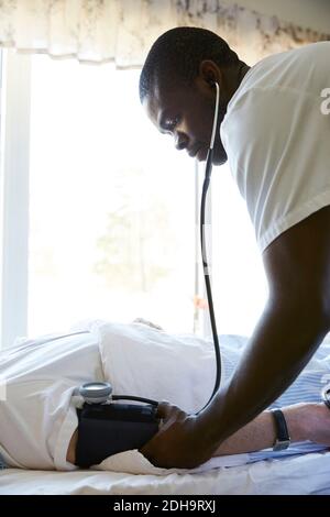 Krankenschwester, die den Blutdruck eines älteren Mannes im Krankenhaus überprüft Bett Stockfoto