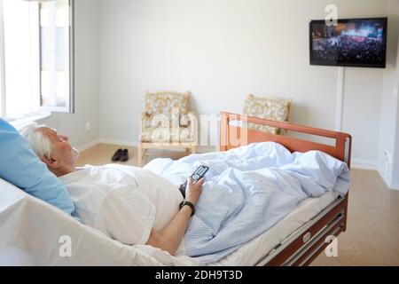 Älterer Mann, der im Krankenhaus Fernsehen schaut, während er sich auf dem Bett zurücklehnend Station Stockfoto