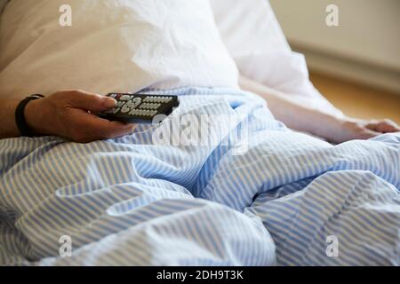 Mittelteil des älteren Mannes mit Fernbedienung auf Krankenhausbett Stockfoto