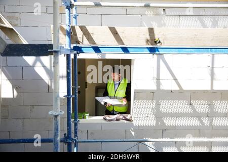 Architekt, der Baupläne analysiert, während er an einem unvollständigen Gebäude steht Stockfoto