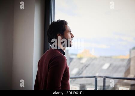 Betrachten Geschäftsmann Blick durch Fenster, während im Büro stehen Stockfoto