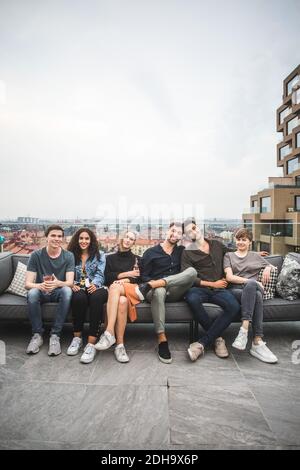 Porträt von lächelnden männlichen und weiblichen Freunden auf dem Sofa sitzen Im Gebäude Terrasse für gesellschaftliche Treffen Stockfoto