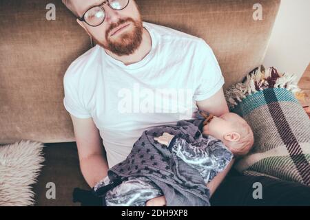 High-Angle-Ansicht des Mannes schlafen, während halten Baby Junge Auf dem Sofa Stockfoto