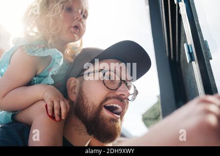 Low-Angle-Ansicht des Vaters reden, während die Tochter auf Schultern an sonnigen Tagen Stockfoto
