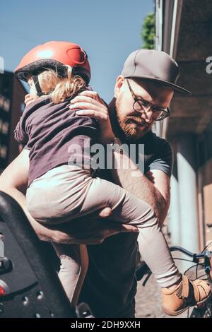 Vater setzen Mädchen auf den Rücksitz des Fahrrads im Freien Stockfoto