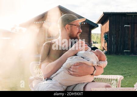 Mittlerer Erwachsener Mann hält Baby Junge, während draußen sitzen Stockfoto